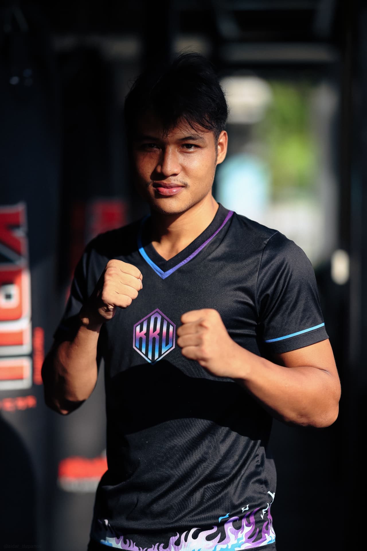 A young KRU fighter holding his guard in front of the heavy bags