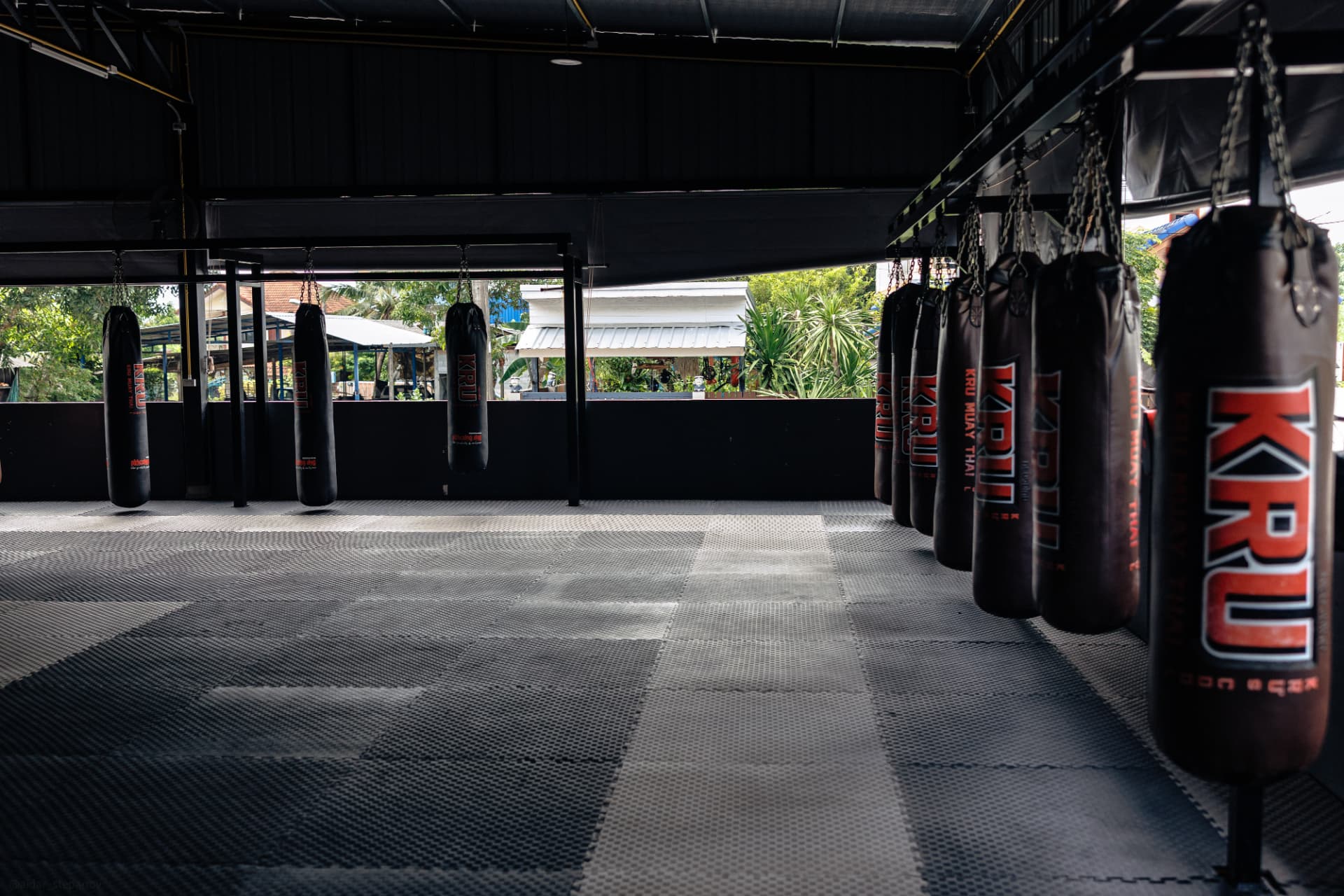 Heavy bags with KRU Muay Thai branding lining the mats
