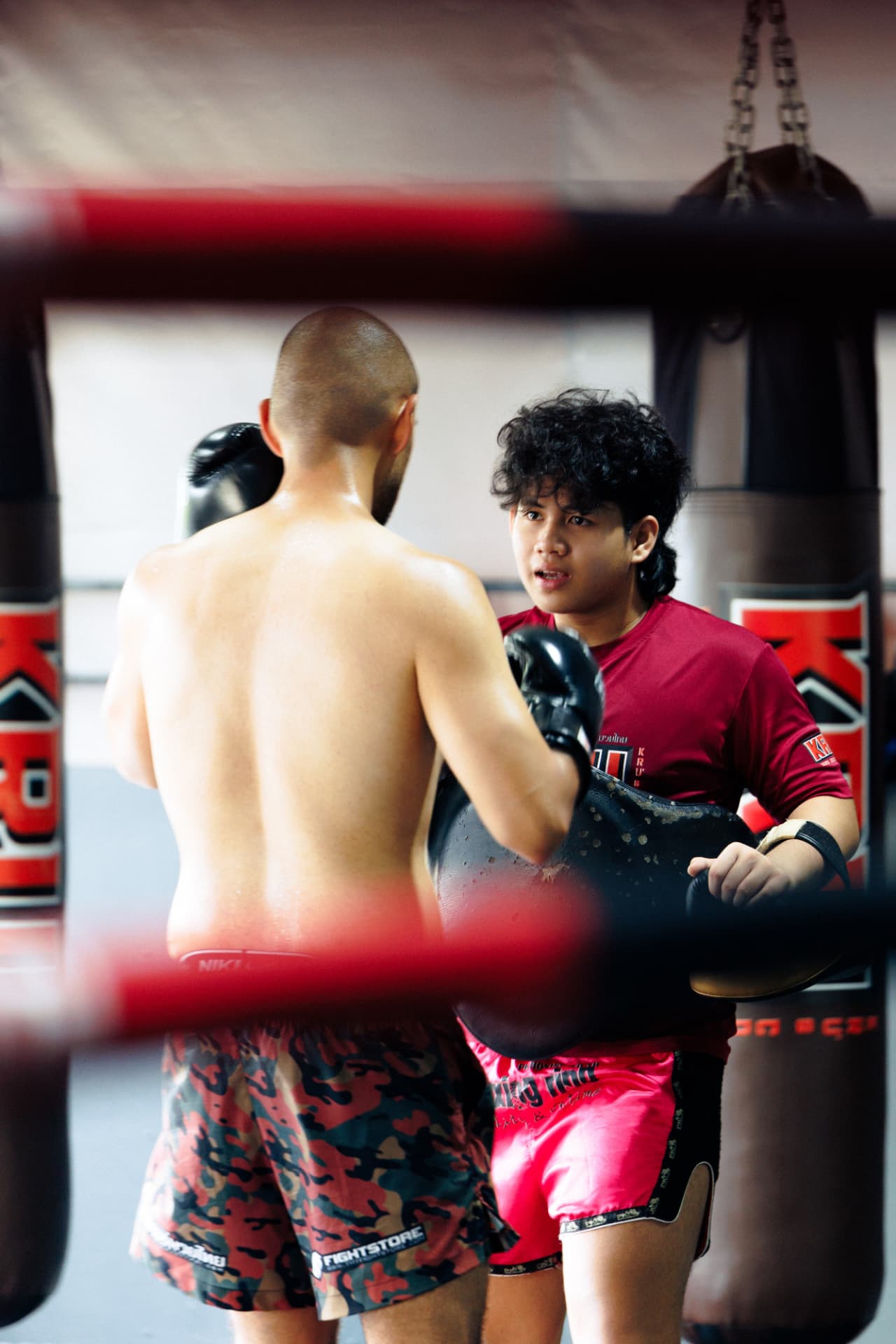 Kru Fino in a red shirt holding a body shield inside the ring