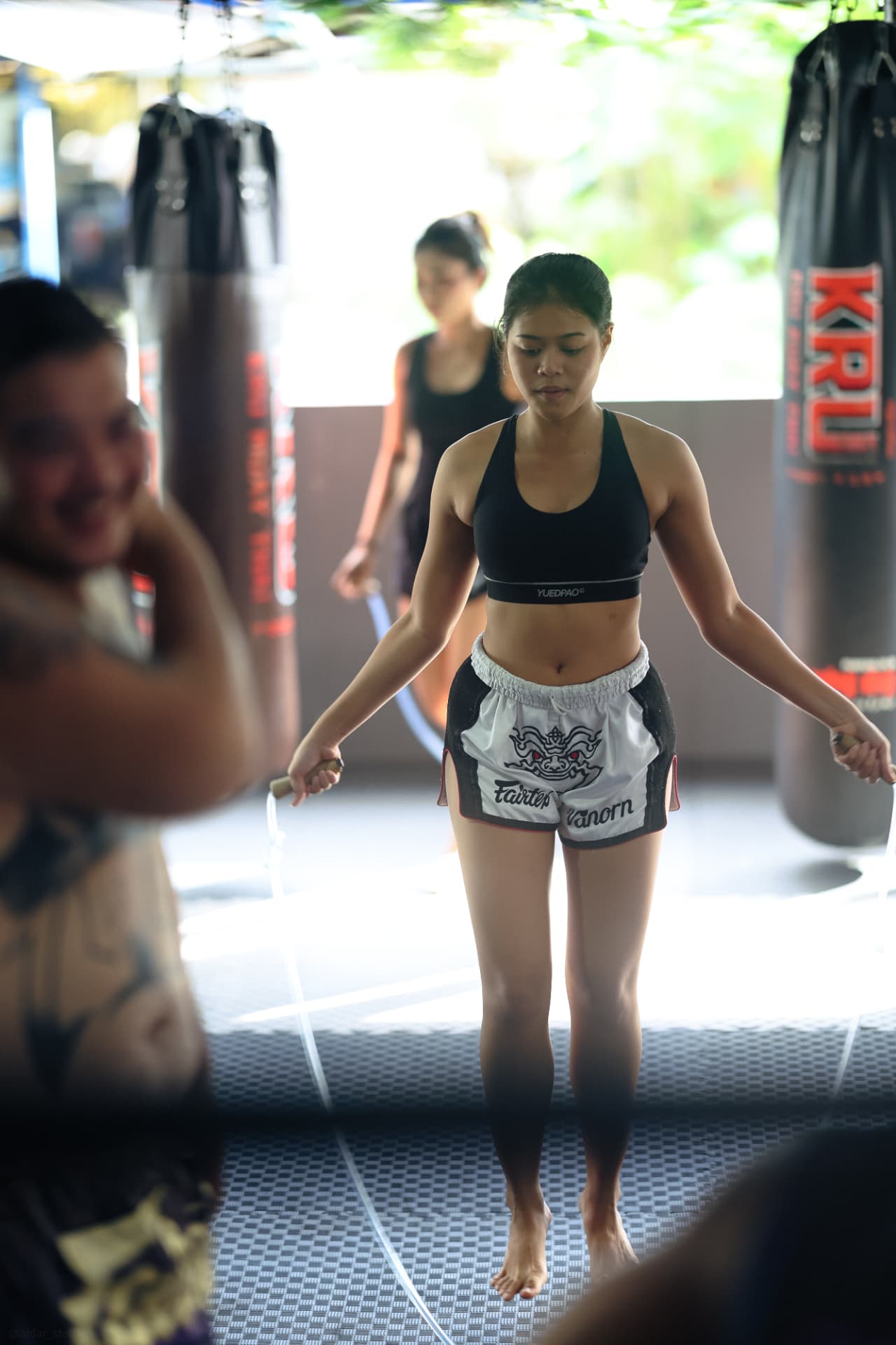 A woman in Muay Thai shorts skipping rope, seen through the ring ropes