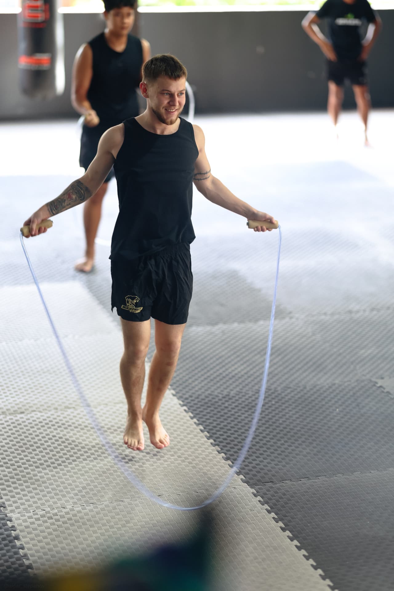 A smiling student in a black tank top skipping rope on the mats