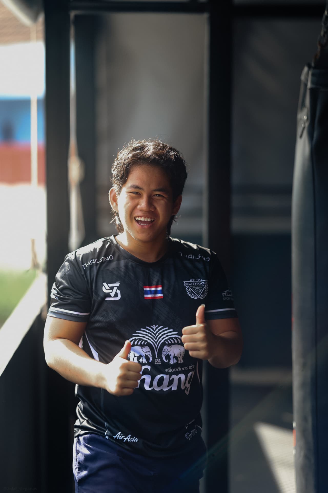 A KRU trainer giving two thumbs up next to the heavy bags