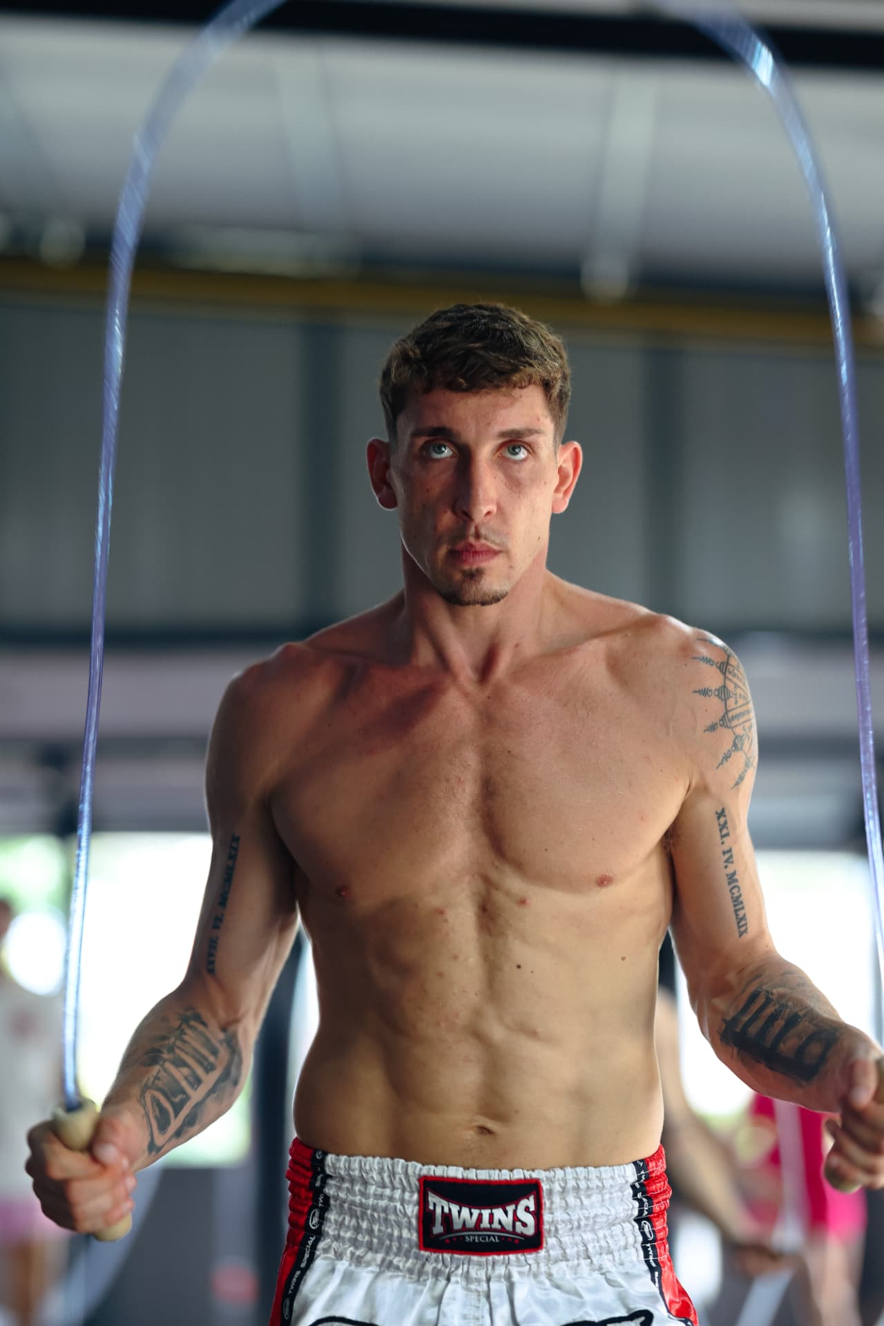 A shirtless fighter in Twins shorts skipping rope and looking at the camera