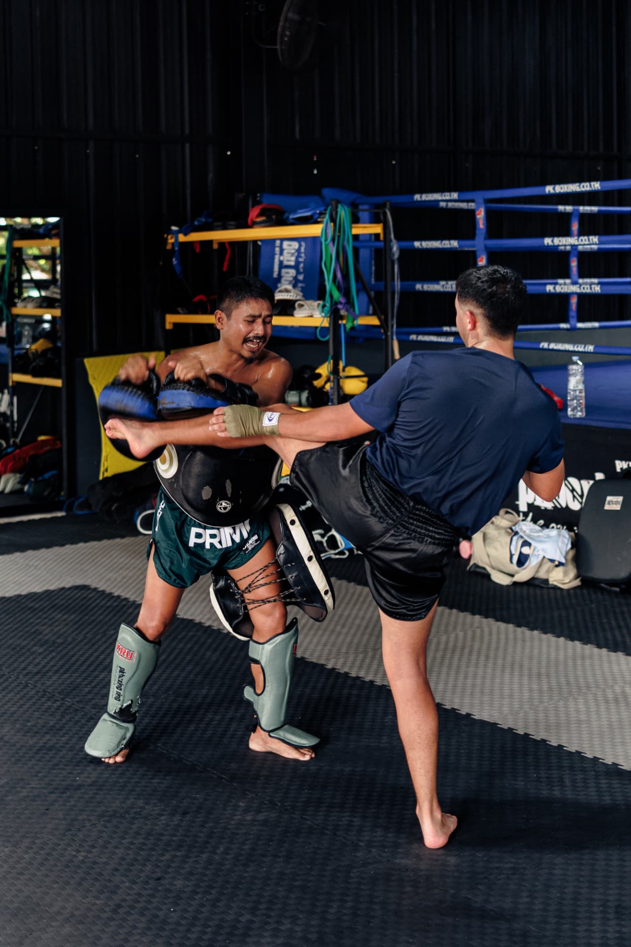 Kru Lai holding focus pads and a body shield as a student lands a kick